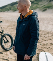 Man at the beach wearing Finisterre's Borealis Waterproof Jacket, made from recycled materials and weatherproof