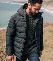 Man in the beach wearing Finisterre's black insulated jacket - the Nebulas - made from 100% recycled fabrics and fill