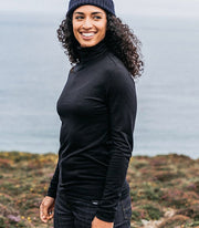 Woman at the beach wearing a cosy black roll neck sweater from Finisterre, made from premium Merino wool blend