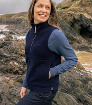 Woman wears a navy fleece gilet made from recycled wool, features side hand pockets and raised neck with half zip